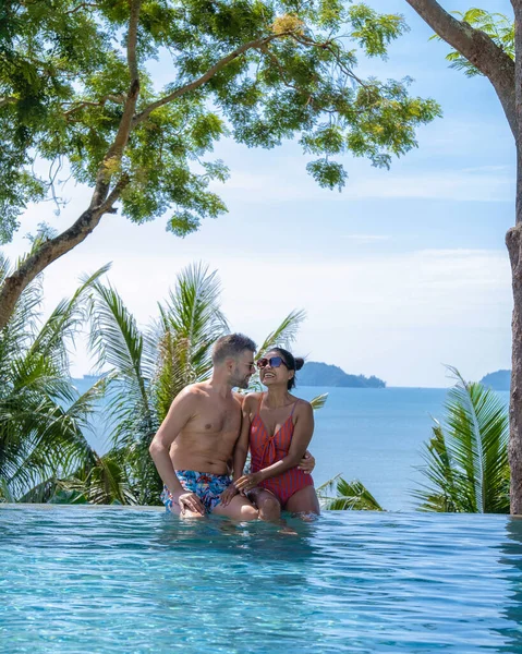 Couple homme et femme d'âge moyen dans la piscine sur des vacances de luxe en Thaïlande, les hommes et la femme asiatique dans la piscine donnant sur la baie en regardant coucher de soleil — Photo