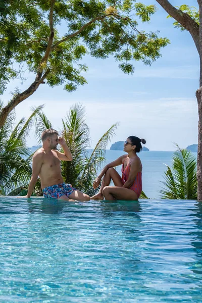 Tayland 'da lüks bir tatilde orta yaşlı bir çiftle yüzme havuzunda erkekler ve Asyalı kadınlar körfeze bakıyor ve gün batımını izliyorlar. — Stok fotoğraf