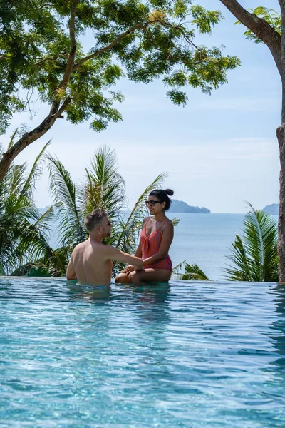 Couple homme et femme d'âge moyen dans la piscine sur des vacances de luxe en Thaïlande, les hommes et la femme asiatique dans la piscine donnant sur la baie en regardant coucher de soleil — Photo