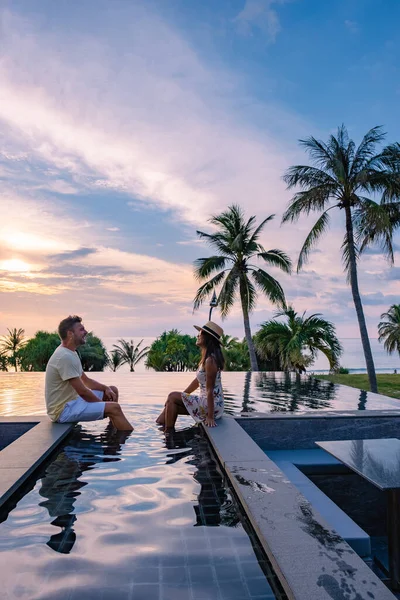 Couple regardant coucher de soleil dans la piscine à débordement sur des vacances de luxe en Thaïlande, homme et femme regardant coucher de soleil sur le bord d'une piscine en Thaïlande — Photo