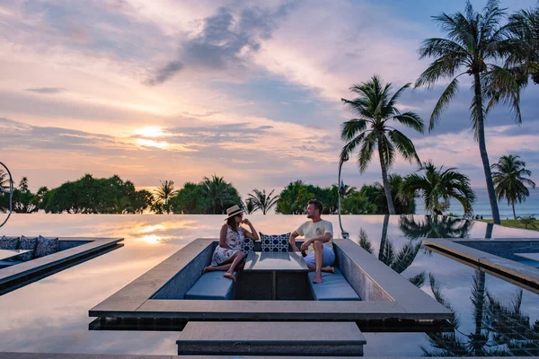 Pareja viendo la puesta de sol en la piscina infinita en unas vacaciones de lujo en Tailandia, hombre y mujer viendo la puesta de sol en el borde de una piscina en Tailandia — Foto de Stock