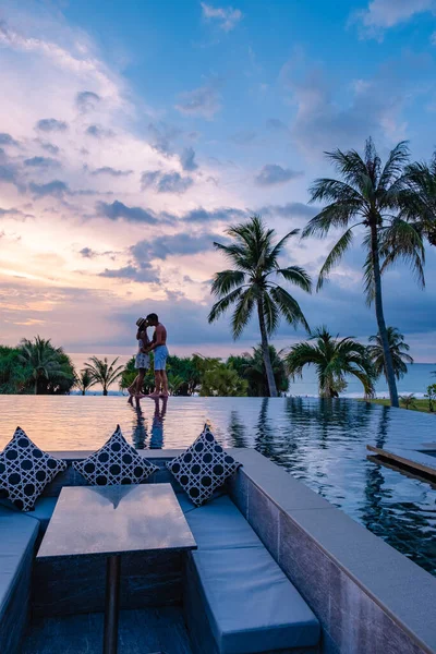 Casal assistindo pôr do sol na piscina infinito em umas férias de luxo na Tailândia, homem e mulher assistindo pôr do sol na borda de uma piscina na Tailândia — Fotografia de Stock