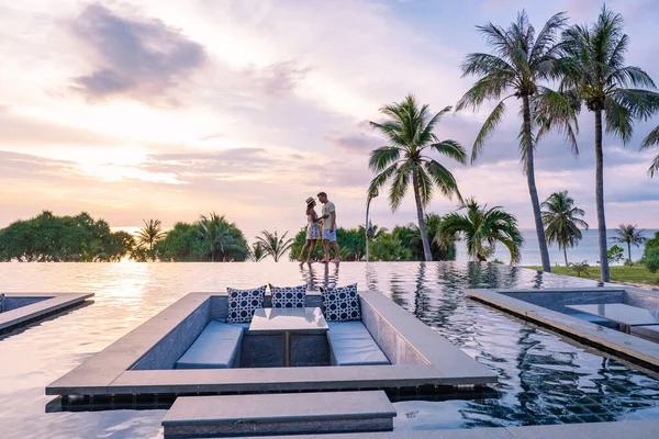 Casal assistindo pôr do sol na piscina infinito em umas férias de luxo na Tailândia, homem e mulher assistindo pôr do sol na borda de uma piscina na Tailândia — Fotografia de Stock