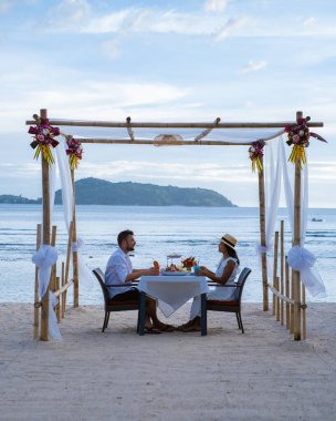 Phuket Tayland 'da kumsalda romantik bir akşam yemeği. Orta yaşlı kadın ve erkek. Orta yaşlı Asyalı kadın ve Avrupalı erkek gün batımında Tayland sahilinde yemek yiyorlar.