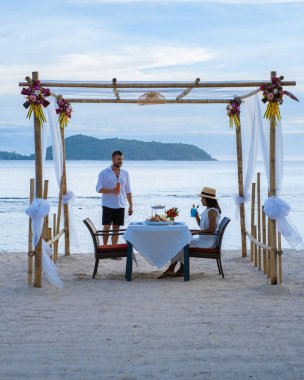 Phuket Tayland 'da kumsalda romantik bir akşam yemeği. Orta yaşlı kadın ve erkek. Orta yaşlı Asyalı kadın ve Avrupalı erkek gün batımında Tayland sahilinde yemek yiyorlar.