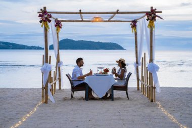 Phuket Tayland 'da kumsalda romantik bir akşam yemeği. Orta yaşlı kadın ve erkek. Orta yaşlı Asyalı kadın ve Avrupalı erkek gün batımında Tayland sahilinde yemek yiyorlar.