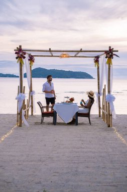 Phuket Tayland 'da kumsalda romantik bir akşam yemeği. Orta yaşlı kadın ve erkek. Orta yaşlı Asyalı kadın ve Avrupalı erkek gün batımında Tayland sahilinde yemek yiyorlar.