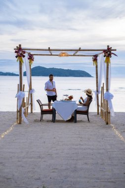 Phuket Tayland 'da kumsalda romantik bir akşam yemeği. Orta yaşlı kadın ve erkek. Orta yaşlı Asyalı kadın ve Avrupalı erkek gün batımında Tayland sahilinde yemek yiyorlar.