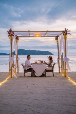 Phuket Tayland 'da kumsalda romantik bir akşam yemeği. Orta yaşlı kadın ve erkek. Orta yaşlı Asyalı kadın ve Avrupalı erkek gün batımında Tayland sahilinde yemek yiyorlar.