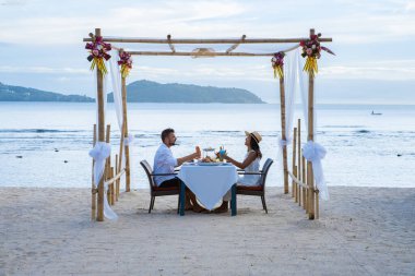 Phuket Tayland 'da kumsalda romantik bir akşam yemeği. Orta yaşlı kadın ve erkek. Orta yaşlı Asyalı kadın ve Avrupalı erkek gün batımında Tayland sahilinde yemek yiyorlar.