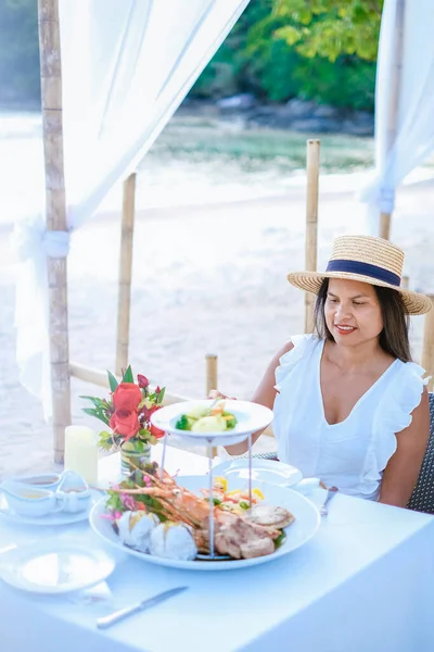 Ρομαντικό δείπνο στην παραλία στο Πουκέτ της Ταϊλάνδης, γυναίκα μέσης ηλικίας ασιατική γυναίκα έχοντας ένα δείπνο στην παραλία στην Ταϊλάνδη κατά τη διάρκεια του ηλιοβασιλέματος — Φωτογραφία Αρχείου