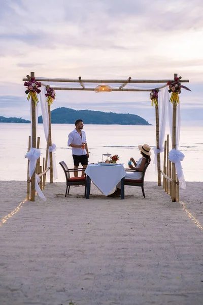 Phuket Tayland 'da kumsalda romantik bir akşam yemeği. Orta yaşlı kadın ve erkek. Orta yaşlı Asyalı kadın ve Avrupalı erkek gün batımında Tayland sahilinde yemek yiyorlar.