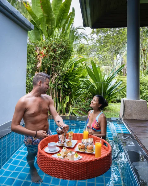 Couple homme et femme avoir flottant petit déjeuner thé élevé dans la piscine en face de leur bungalow — Photo