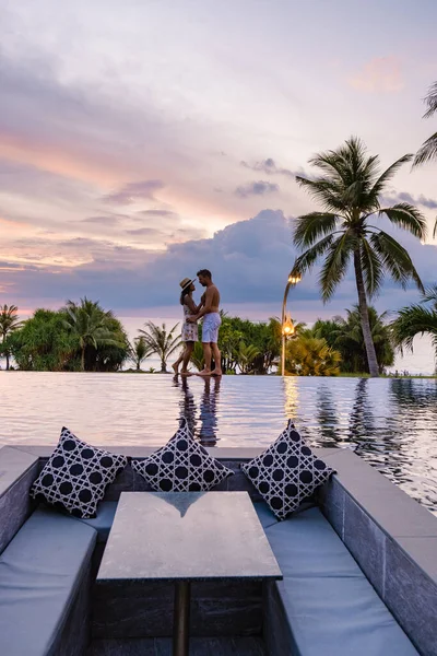 Pareja hombre y mujer viendo la puesta de sol desde una piscina infinita en la azotea en unas vacaciones de lujo —  Fotos de Stock