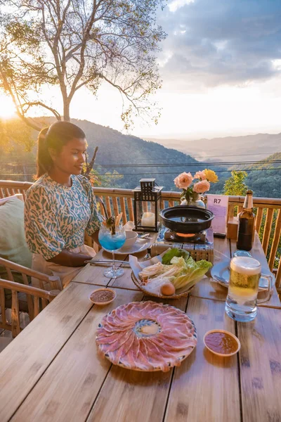 Dinner in the mountains of Chiang Mai Thailand, table bbq, Asian man using kitchen tongs grilling beef and bacon on grill plate. Eating Korean Barbecue buffet in the restaurant. — 스톡 사진