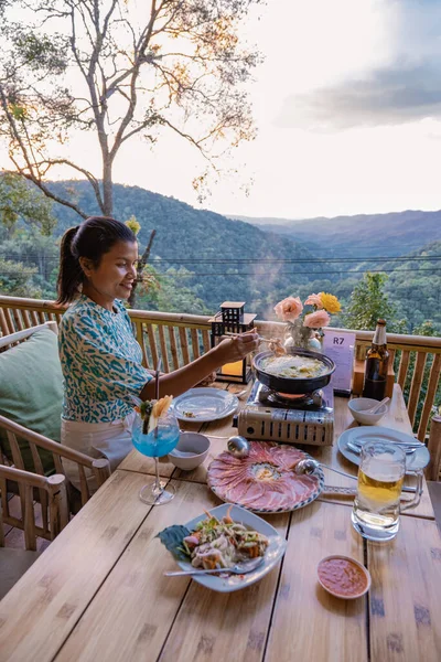Dinner in the mountains of Chiang Mai Thailand, table bbq, Asian man using kitchen tongs grilling beef and bacon on grill plate. Eating Korean Barbecue buffet in the restaurant. — Fotografia de Stock