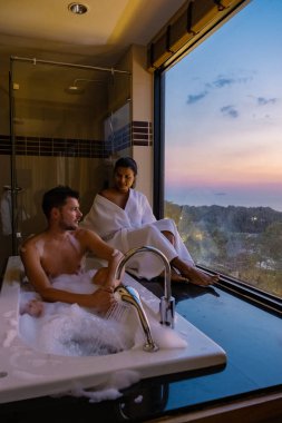 Gündoğumunda banyo yapan çift, gün batımında otel odasında Avrupalı erkek ve Asyalı kadın.