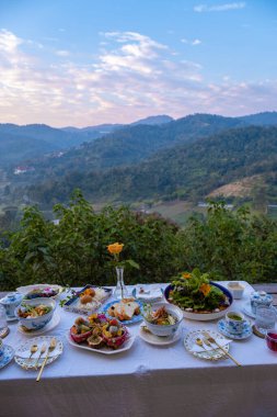 Tayland 'ın dağlarında kahvaltı masası, ahşap masa ev yapımı yiyecek ve içeceklerle güneşli bir günde çam ağacının altında taze meyve ve çiçeklerle servis edilir. Lüks kahvaltı.