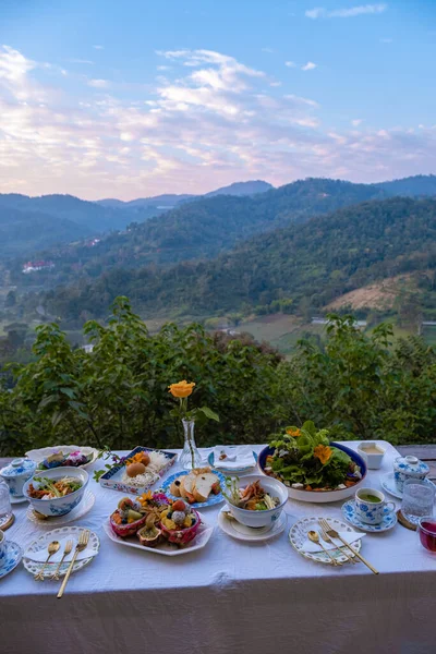 Table de petit déjeuner dans les montagnes de Thaïlande Chiang Mai, table de fête en bois servi avec de la nourriture et des boissons maison, des fruits frais et des fleurs sous le pin par une journée ensoleillée. Petit déjeuner de luxe — Photo