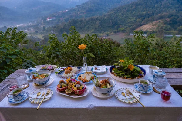 Tavolo per la colazione nelle montagne della Thailandia Chiang Mai, tavolo festivo in legno servito con cibi e bevande fatti in casa, frutta fresca e fiori sotto il pino nella giornata di sole. Colazione di lusso — Foto Stock