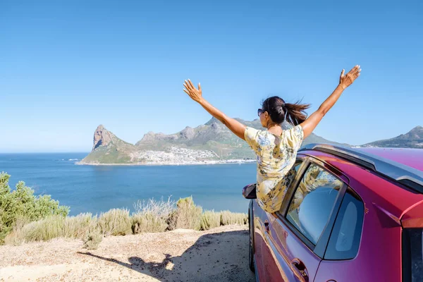 Kobieta przed oknem samochodu wycieczka z rękami w górze, samochód na Chapmans Peak Drive w Kapsztadzie RPA z widokiem na ocean — Zdjęcie stockowe