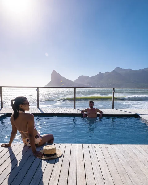 Coppia uomo e donna di fronte alla piscina Infinity affacciata sull'oceano di Città del Capo Sud Africa, uomo e donna in piscina durante il tramonto — Foto Stock