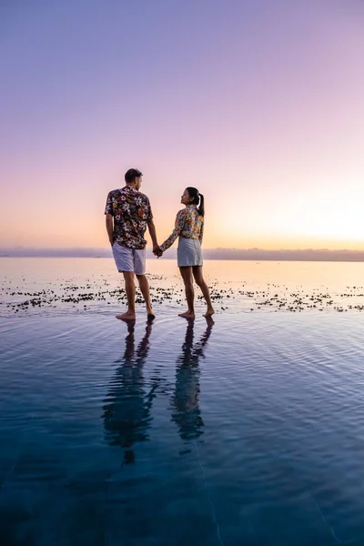 Pareja de hombres y mujeres frente a la piscina Infinity con vistas al océano de Ciudad del Cabo Sudáfrica, hombres y mujeres en la piscina al atardecer — Foto de Stock