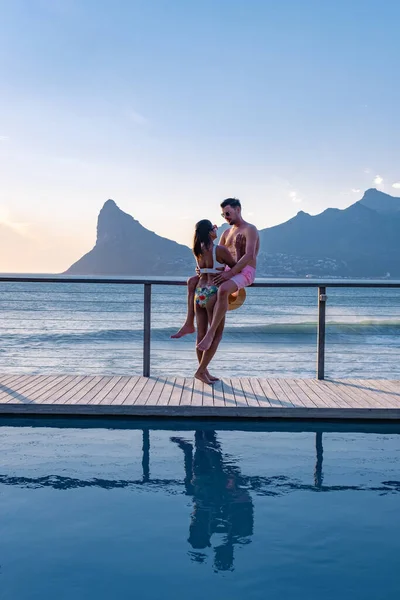 Coppia uomo e donna di fronte alla piscina Infinity affacciata sull'oceano di Città del Capo Sud Africa, uomo e donna in piscina durante il tramonto — Foto Stock