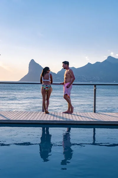 Coppia uomo e donna di fronte alla piscina Infinity affacciata sull'oceano di Città del Capo Sud Africa, uomo e donna in piscina durante il tramonto — Foto Stock