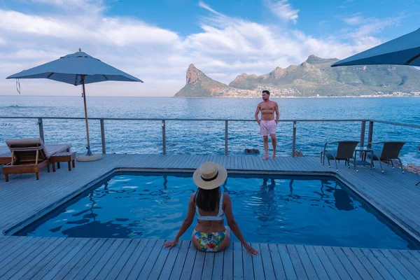 Ζευγάρι άνδρας και γυναίκα μπροστά από Infinity πισίνα με θέα στον ωκεανό του Κέιπ Τάουν της Νότιας Αφρικής, άνδρας και γυναίκα στην πισίνα κατά τη διάρκεια του ηλιοβασιλέματος — Φωτογραφία Αρχείου