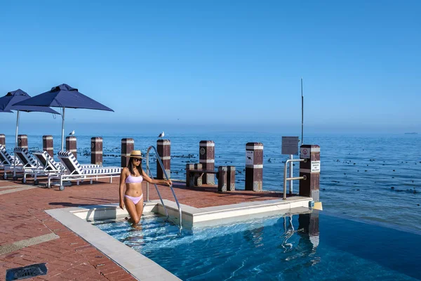 Mujer frente a la piscina Infinity con vistas al océano de Ciudad del Cabo Sudáfrica, hombre y mujer en la piscina al atardecer — Foto de Stock