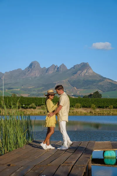在南非开普敦附近的斯泰伦博希，一对男女从湖面眺望，夕阳西下的葡萄园与群山交相辉映 — 图库照片