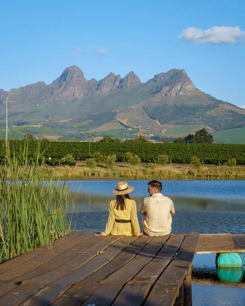 Pareja de hombres y mujeres mirando hacia el lago, Paisaje del viñedo al atardecer con montañas en Stellenbosch, cerca de Ciudad del Cabo, Sudáfrica — Foto de Stock