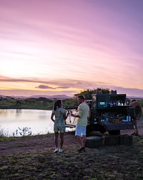 Para mężczyzn i kobiet oglądających zachód słońca podczas safar game drive w RPA, zachód słońca nad jeziorem w basenie wodnym w Savannah Południowej Afryki Kwazulu Natal — Zdjęcie stockowe