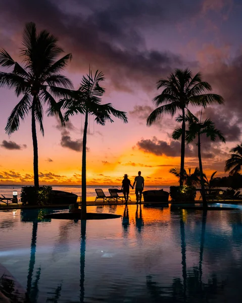 Naplemente trópusi medence pálmafákkal, pár férfi és nő nézi naplementét a medence pálmafákkal nyaralás közben Mauritius — Stock Fotó