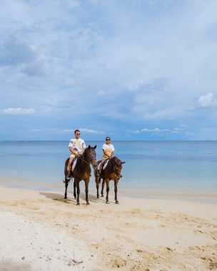 Sahilde ata binen adam ve kadın, Mauritius 'ta lüks bir tatil sırasında sahilde ata biniyorlar.