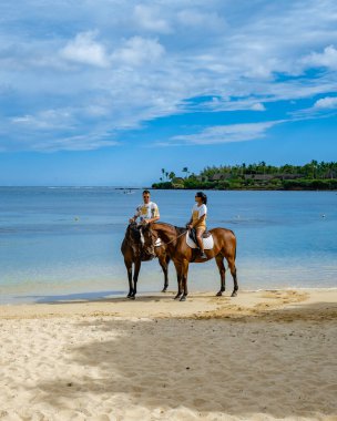 Sahilde ata binen adam ve kadın, Mauritius 'ta lüks bir tatil sırasında sahilde ata biniyorlar.