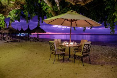 Mauritius sahilinde gün batımı. Şemsiyeli lüks bir restoran ve akşam yemeği için sahilde sandalyeler.