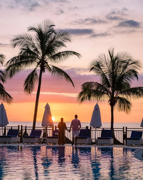 Pareja hombre y mujer viendo atardecer en una piscina con palmeras tropicales durante unas vacaciones de lujo —  Fotos de Stock