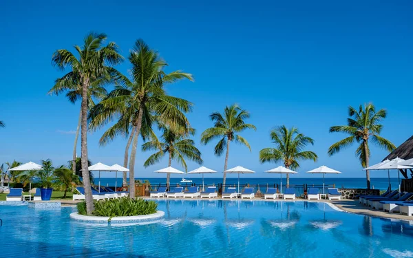 Pięknych tropikalnych przy plaży ośrodek z basenem, leżakami i dłoń drzewa w ciepły słoneczny dzień, przeznaczenia raj na wakacje — Zdjęcie stockowe