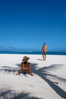 Palmiye ağaçları, beyaz kum mavisi okyanus ve şemsiyeli plaj yatakları, güneş sandalyeleri ve güneş şemsiyeleri tropikal bir beac olan Le Morne plajı Mauritius 'taki palmiye ağacının altında.