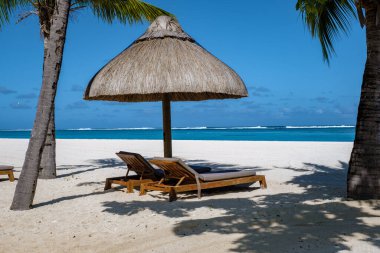 Palmiye ağaçları, beyaz kum mavisi okyanus ve şemsiyeli plaj yatakları, güneş sandalyeleri ve güneş şemsiyeleri tropikal bir beac olan Le Morne plajı Mauritius 'taki palmiye ağacının altında.
