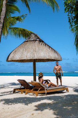 Palmiye ağaçları, beyaz kum mavisi okyanus ve şemsiyeli plaj yatakları, güneş sandalyeleri ve güneş şemsiyeleri tropikal bir beac olan Le Morne plajı Mauritius 'taki palmiye ağacının altında.