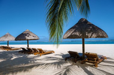 Palmiye ağaçları, beyaz kum mavisi okyanus ve şemsiyeli plaj yatakları, güneş sandalyeleri ve güneş şemsiyeleri tropikal bir beac olan Le Morne plajı Mauritius 'taki palmiye ağacının altında.