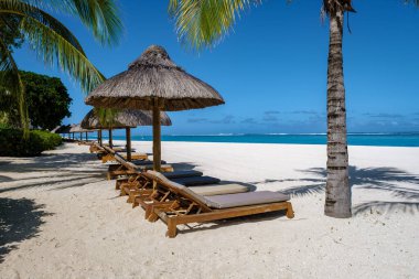 Palmiye ağaçları, beyaz kum mavisi okyanus ve şemsiyeli plaj yatakları, güneş sandalyeleri ve güneş şemsiyeleri tropikal bir beac olan Le Morne plajı Mauritius 'taki palmiye ağacının altında.