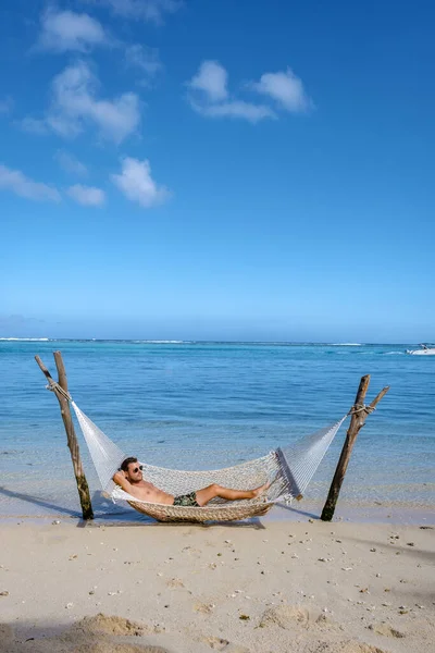 Tropical beach with hammock in the ocean, white sandy beach with hammock Le Morne beach Mauritius, young men in hammock — Zdjęcie stockowe