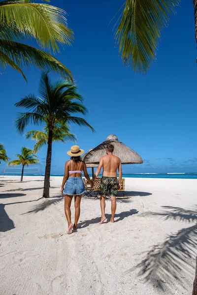 Palmiye ağaçları, beyaz kum mavisi okyanus ve şemsiyeli plaj yatakları, güneş sandalyeleri ve güneş şemsiyeleri tropikal bir beac olan Le Morne plajı Mauritius 'taki palmiye ağacının altında.