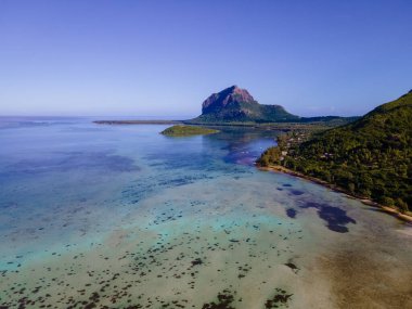 Le Morne plajı Mauritius, Tropikal plaj palmiye ağaçları ve beyaz kum mavisi okyanus ve şemsiyeli plaj yatakları, güneş sandalyeleri ve güneş şemsiyeleri bir palmiye ağacının altında, Le Morne plajı Mauritius 'ta.