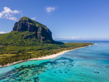 Le Morne plajı Mauritius, Tropikal plaj palmiye ağaçları ve beyaz kum mavisi okyanus ve şemsiyeli plaj yatakları, güneş sandalyeleri ve güneş şemsiyeleri bir palmiye ağacının altında, Le Morne plajı Mauritius 'ta.