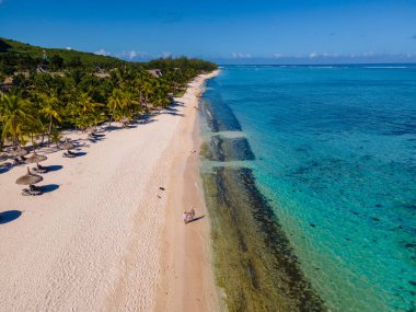 Le Morne plajı Mauritius, Tropikal plaj palmiye ağaçları ve beyaz kum mavisi okyanus. Tatil sırasında sahilde yürüyen çift ve kadın.